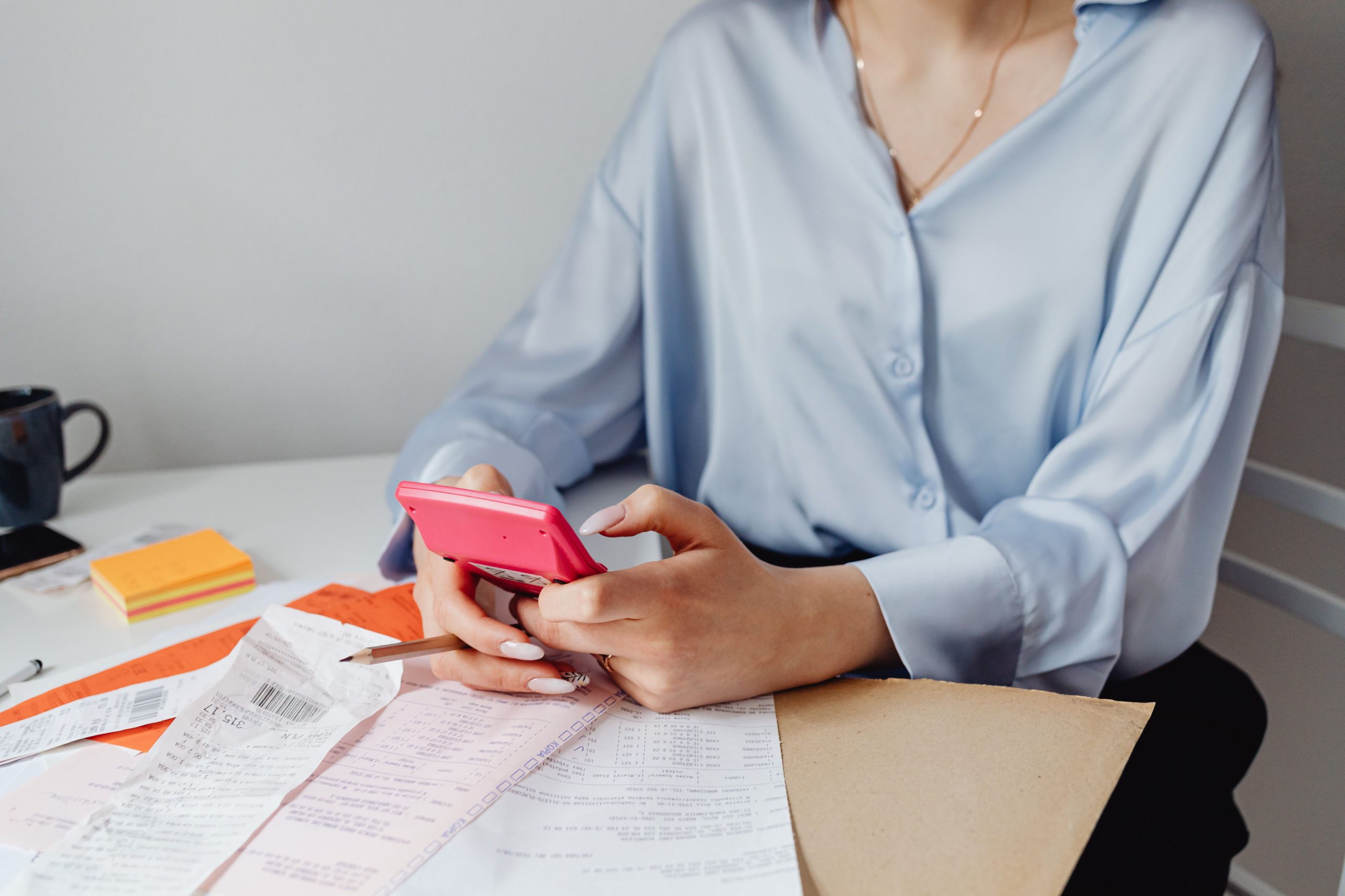 Person using a calculator while reviewing bills, receipts and household expenses at a desk.
