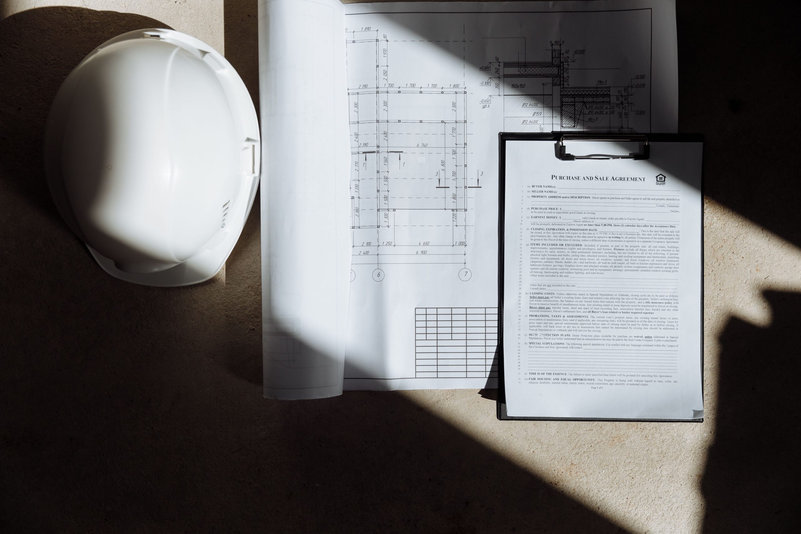 Construction plans and a property contract beside a hard hat on a building site.